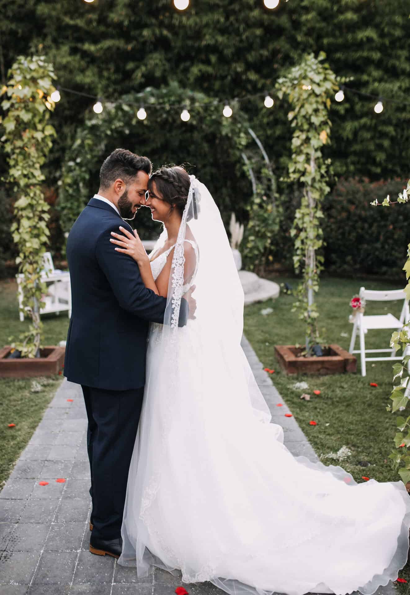 Novios bajo arco floral iluminado en ceremonia nocturna de boda